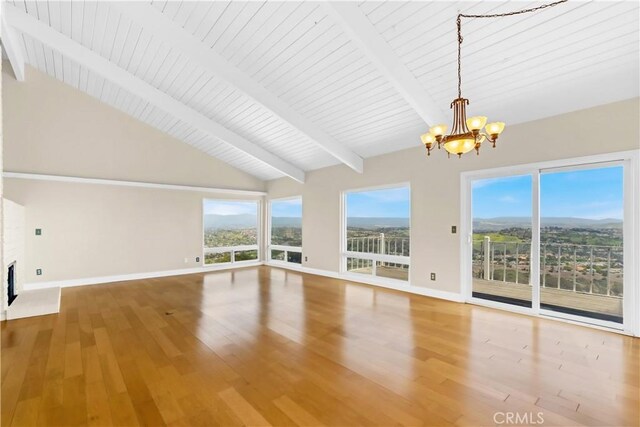unfurnished living room with a chandelier, baseboards, beamed ceiling, wood finished floors, and healthy amount of natural light