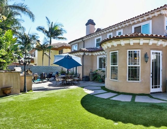 back of house with a patio area, stucco siding, a yard, and a chimney