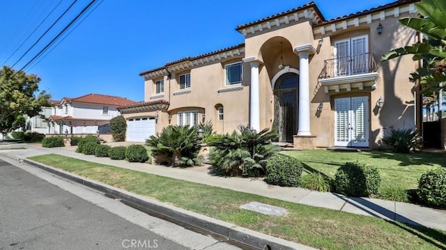 mediterranean / spanish home with an attached garage, a front lawn, stucco siding, a balcony, and french doors