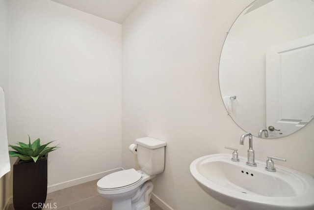 half bathroom with a sink, baseboards, tile patterned floors, and toilet