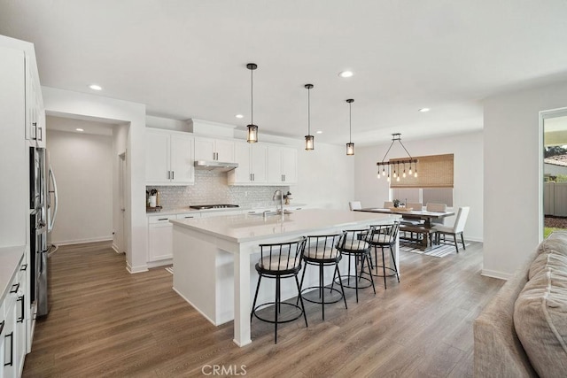 kitchen with gas cooktop, light wood-style floors, a breakfast bar area, recessed lighting, and under cabinet range hood