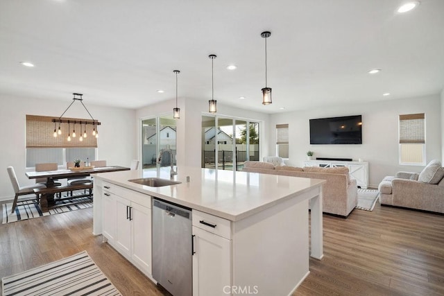 kitchen with a sink, light wood-style floors, a kitchen island with sink, white cabinetry, and stainless steel dishwasher
