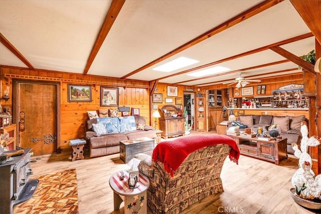 living area featuring beamed ceiling, a ceiling fan, wood walls, and wood finished floors