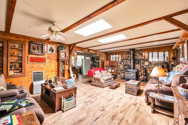 living area with wooden walls, a ceiling fan, a wood stove, and hardwood / wood-style floors