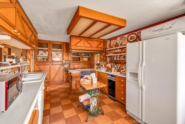 kitchen featuring a sink, light countertops, brown cabinetry, white fridge with ice dispenser, and stainless steel microwave