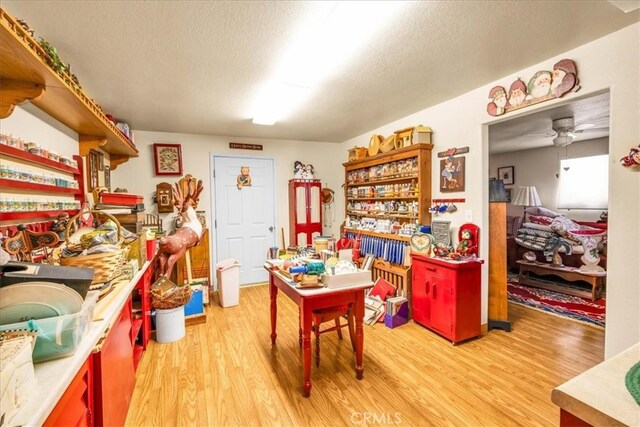 recreation room featuring a ceiling fan, light wood finished floors, and a textured ceiling