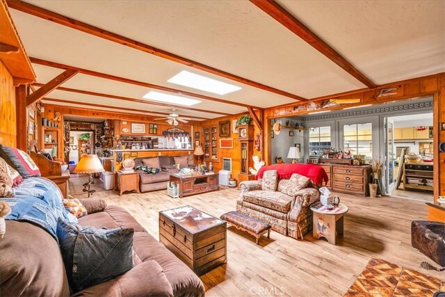 living room featuring wooden walls, ceiling fan, beamed ceiling, and wood finished floors