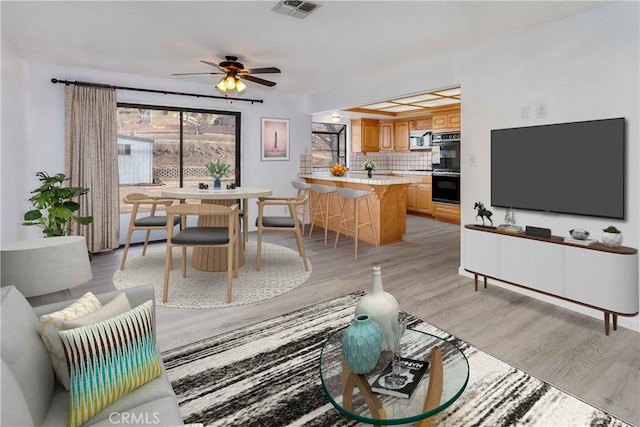 living room featuring visible vents, light wood-style flooring, and ceiling fan