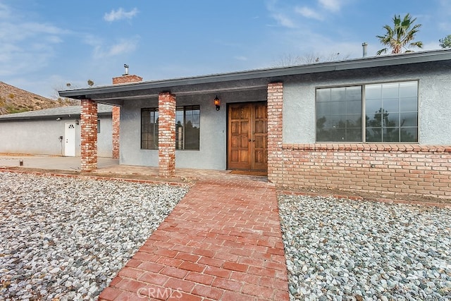 single story home featuring stucco siding, covered porch, and a chimney