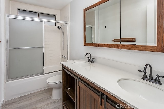bathroom featuring a sink, combined bath / shower with glass door, toilet, and wood finished floors