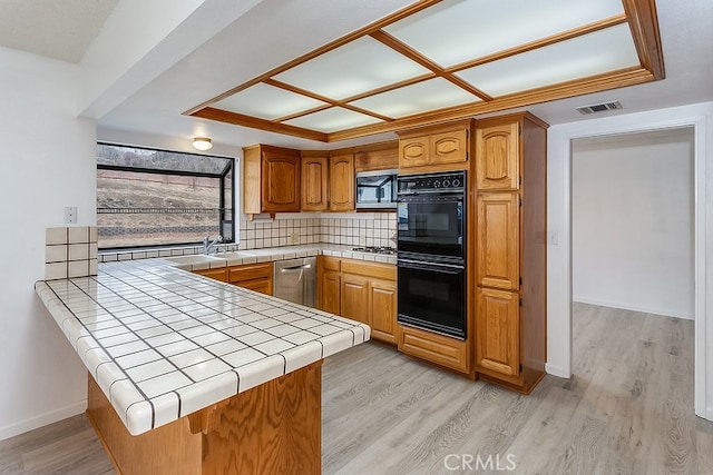 kitchen with tile countertops, tasteful backsplash, light wood-type flooring, a peninsula, and stainless steel appliances