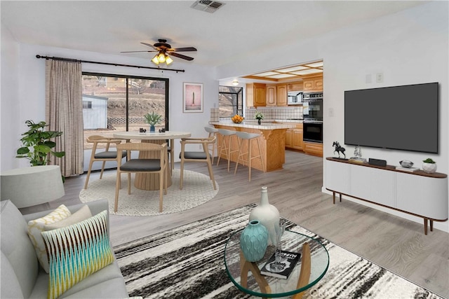 living room with ceiling fan, visible vents, and light wood finished floors