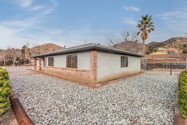 view of home's exterior featuring fence, a mountain view, stucco siding, and brick siding