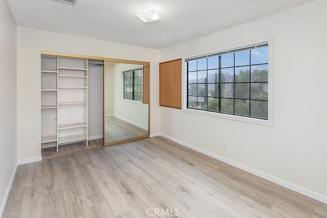 unfurnished bedroom featuring a closet, a textured ceiling, baseboards, and light wood-style floors