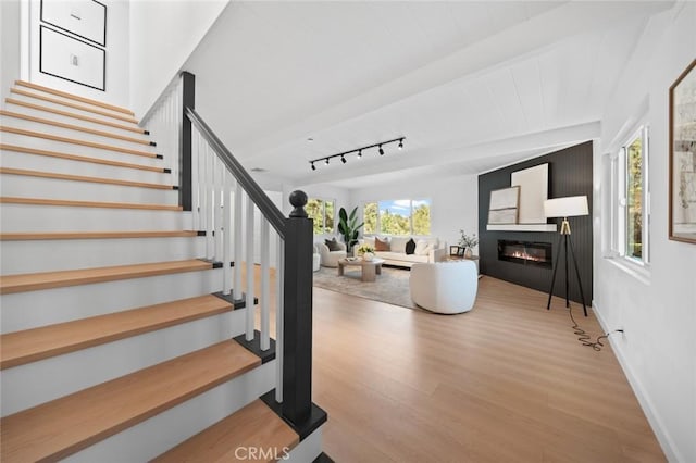 staircase featuring a glass covered fireplace, baseboards, and wood finished floors