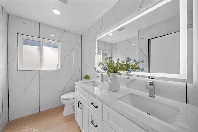 bathroom featuring a sink, toilet, double vanity, and wood finished floors