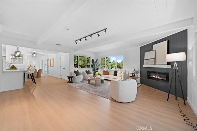 living room featuring visible vents, beam ceiling, light wood-style floors, a large fireplace, and rail lighting