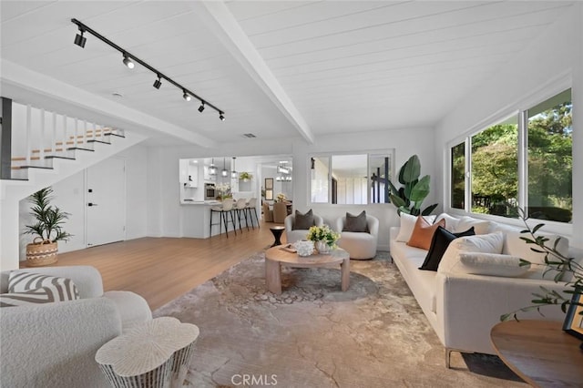 living room with track lighting, light wood finished floors, stairs, and beamed ceiling