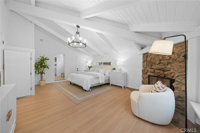 bedroom with an inviting chandelier, vaulted ceiling with beams, light wood finished floors, and a fireplace