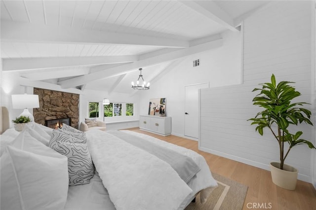 bedroom with visible vents, a stone fireplace, vaulted ceiling with beams, light wood-style flooring, and a notable chandelier