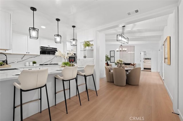 kitchen with a breakfast bar area, visible vents, a sink, white cabinets, and light wood-style floors