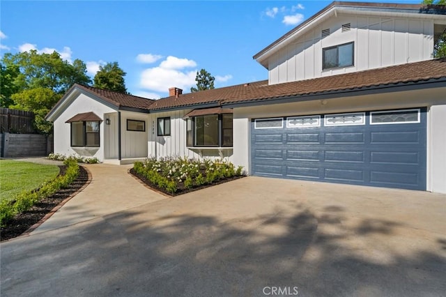 view of front facade featuring fence, a chimney, board and batten siding, driveway, and a tile roof