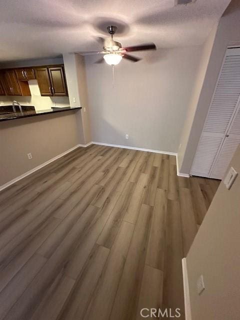 unfurnished living room featuring a sink, baseboards, ceiling fan, and dark wood-type flooring