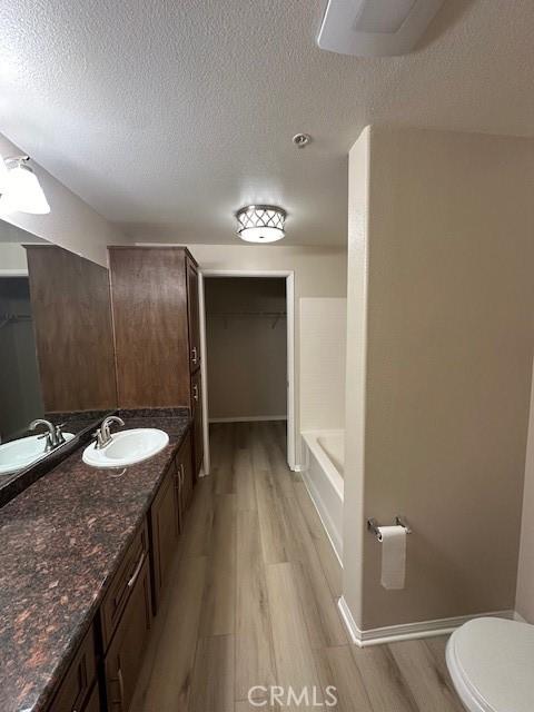 bathroom featuring vanity, wood finished floors, toilet, walk in shower, and a textured ceiling