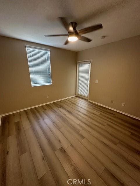 empty room featuring a healthy amount of sunlight, baseboards, a ceiling fan, and wood finished floors