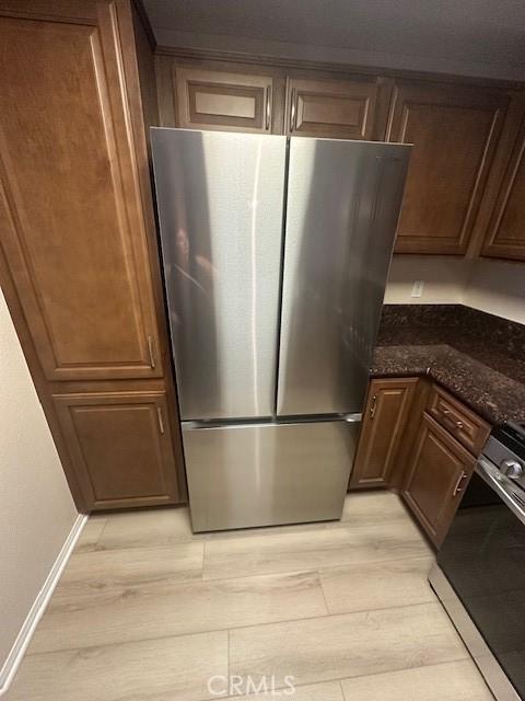 kitchen featuring stove, dark stone countertops, freestanding refrigerator, baseboards, and light wood-type flooring