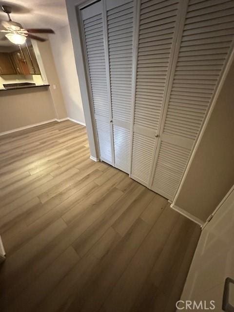 unfurnished bedroom featuring baseboards, ceiling fan, light wood finished floors, and a closet