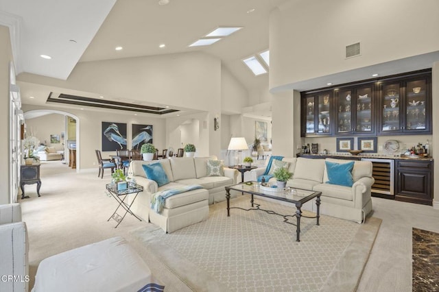 carpeted living room with high vaulted ceiling, visible vents, arched walkways, beverage cooler, and bar area