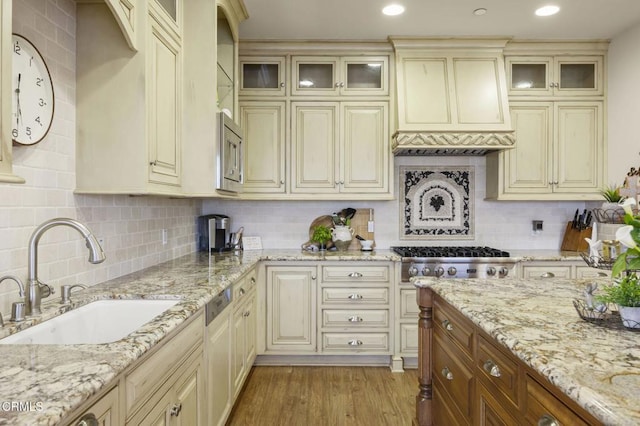 kitchen featuring glass insert cabinets, a sink, cream cabinetry, backsplash, and stainless steel appliances