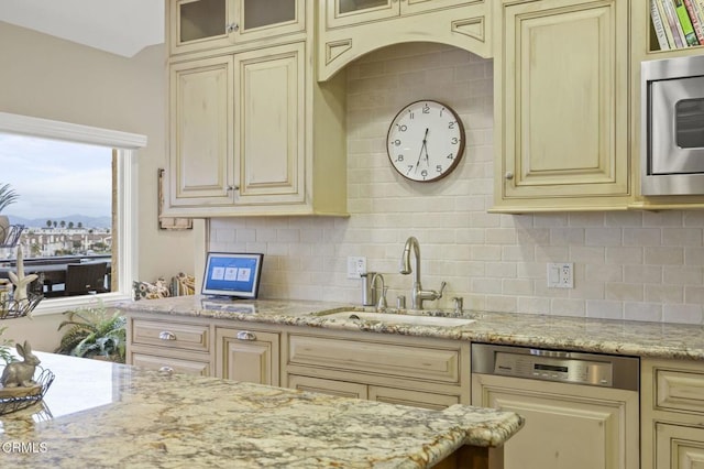 kitchen featuring glass insert cabinets, dishwasher, stainless steel microwave, a sink, and cream cabinets