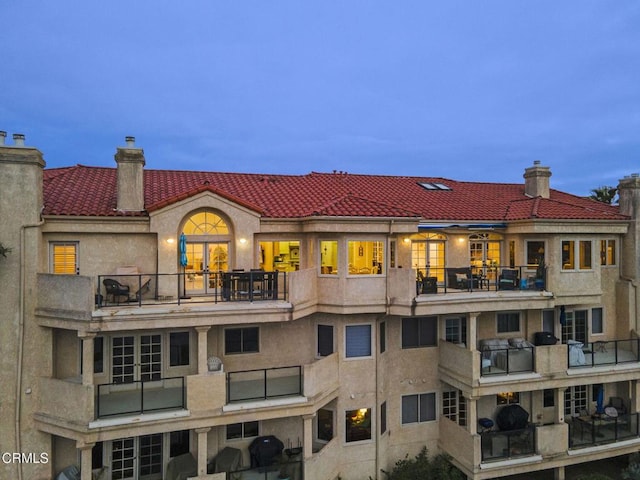 rear view of house featuring stucco siding, a tiled roof, a chimney, and a balcony