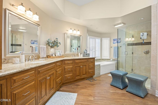 bathroom featuring a sink, a shower stall, a garden tub, double vanity, and wood finished floors