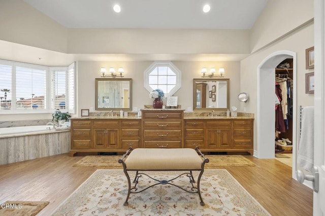 full bathroom with a walk in closet, a garden tub, double vanity, and wood finished floors