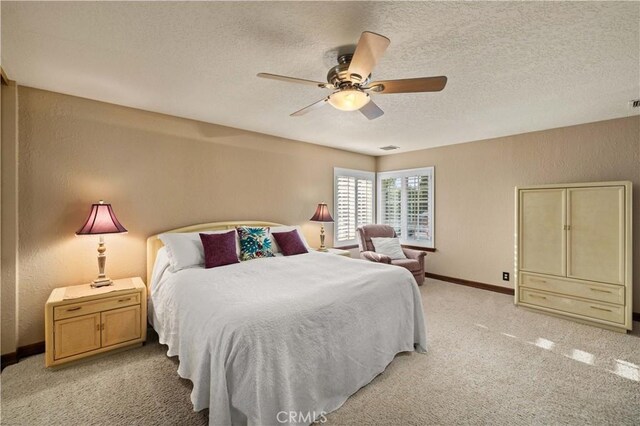 bedroom featuring a ceiling fan, a textured ceiling, light colored carpet, baseboards, and a textured wall