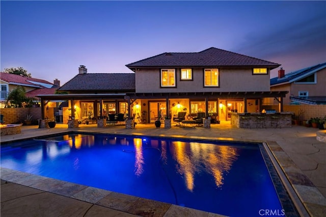 pool at dusk with fence, outdoor dry bar, an outdoor fire pit, a fenced in pool, and a patio area