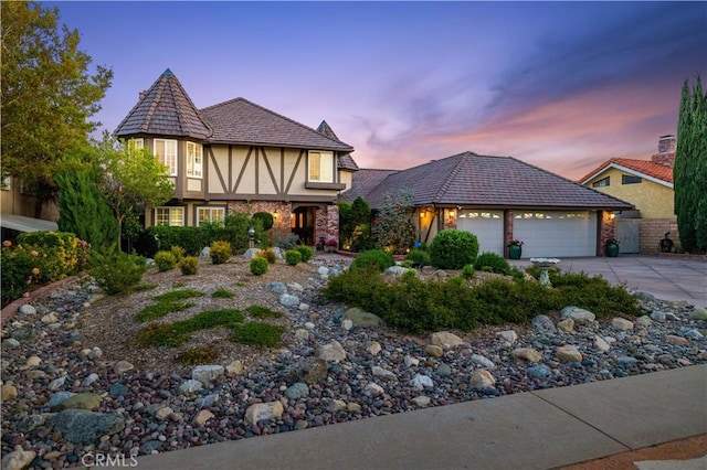 tudor home featuring a garage, stucco siding, and driveway