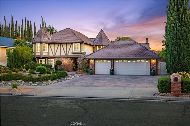 tudor house with an attached garage, brick siding, stucco siding, a chimney, and driveway