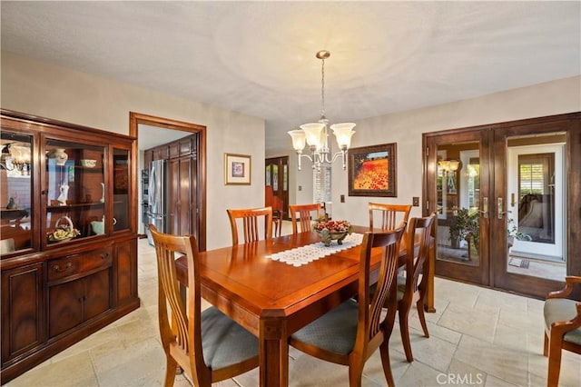 dining space with french doors, stone tile floors, and a notable chandelier