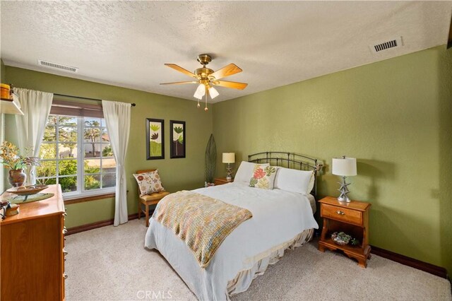 carpeted bedroom featuring a textured ceiling, baseboards, visible vents, and a ceiling fan