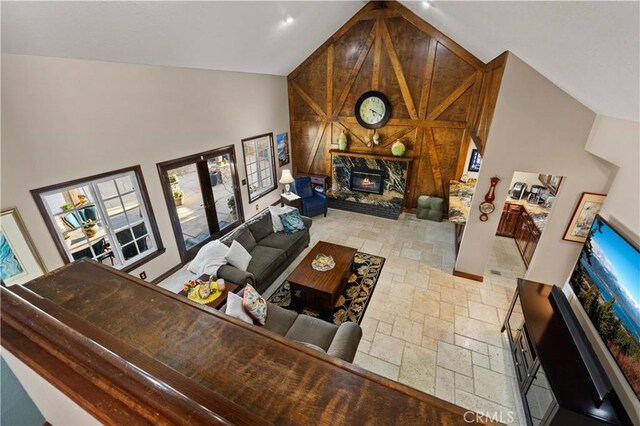 living room with a fireplace, high vaulted ceiling, wood walls, french doors, and stone tile floors