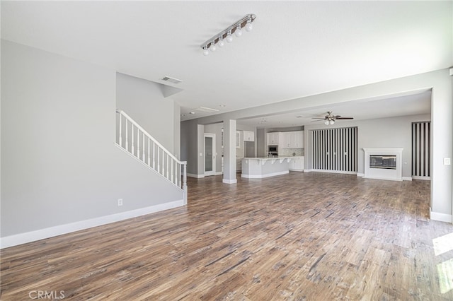 unfurnished living room featuring visible vents, stairs, a glass covered fireplace, wood finished floors, and baseboards