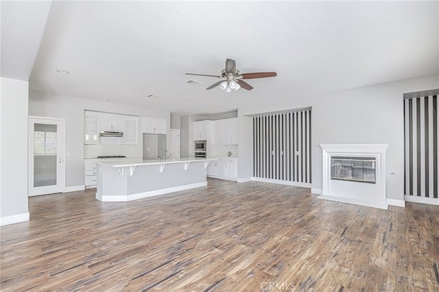 unfurnished living room featuring visible vents, a fireplace with flush hearth, wood finished floors, baseboards, and a ceiling fan
