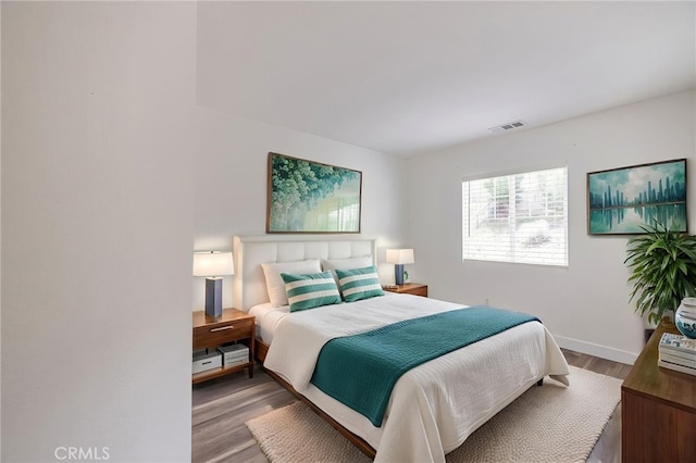 bedroom with baseboards, visible vents, and wood finished floors