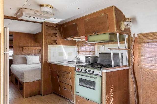 kitchen featuring decorative backsplash, extractor fan, gas range oven, a sink, and light wood-style flooring
