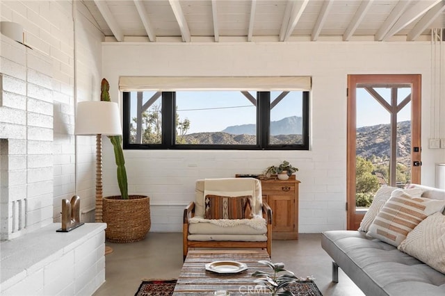 sitting room featuring finished concrete flooring, a mountain view, a wealth of natural light, and beamed ceiling