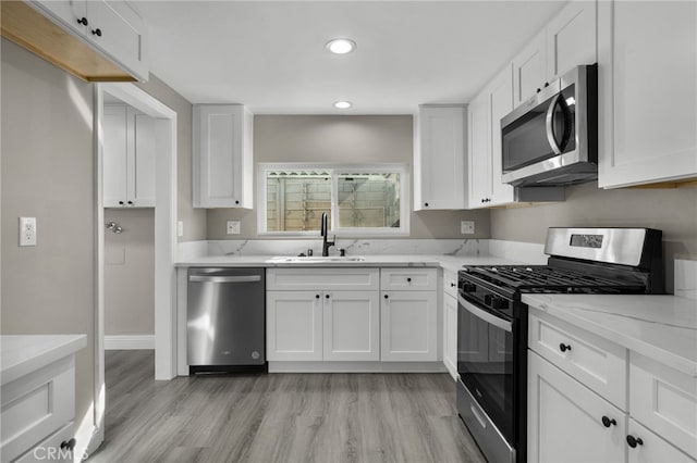 kitchen featuring white cabinetry, appliances with stainless steel finishes, a sink, and light wood-type flooring